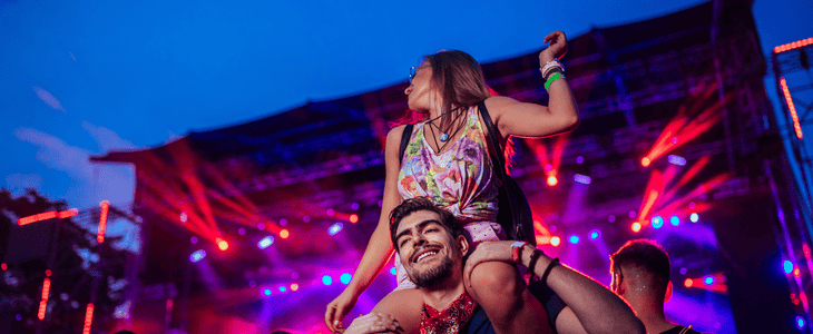 A pair of festival attendees smile while a man holds his girlfriend up to see the stage